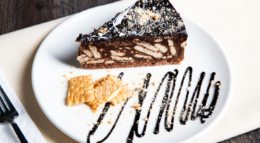 Close up slice of no-bake chocolate biscuit cake showing biscuit chunks and fudgy texture on a rustic ceramic plate.