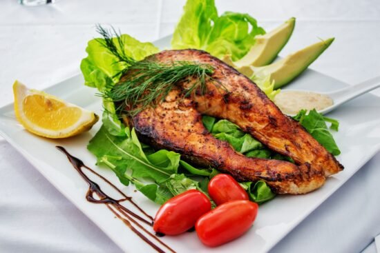 HAND HOLDING AIR FRYER BASKET WITH TWO SLICES OF RAW SALMON READY TO COOK IN TH